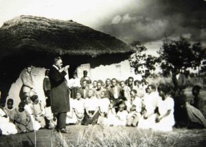 sch 0035. Rev. Hans Astrup preaching at a Sunday morning service at Tabor. Sch 0035 "Pastor Hans Astrup holder gudstjeneste". ("Rev Hans Astrup holding a Sunday Service"). Rev Ylvisaker standing up against the wall. The place is called Tabor. Picture in book: "Unkulunkulu in Zululand" by Andrew Burgess, 1934